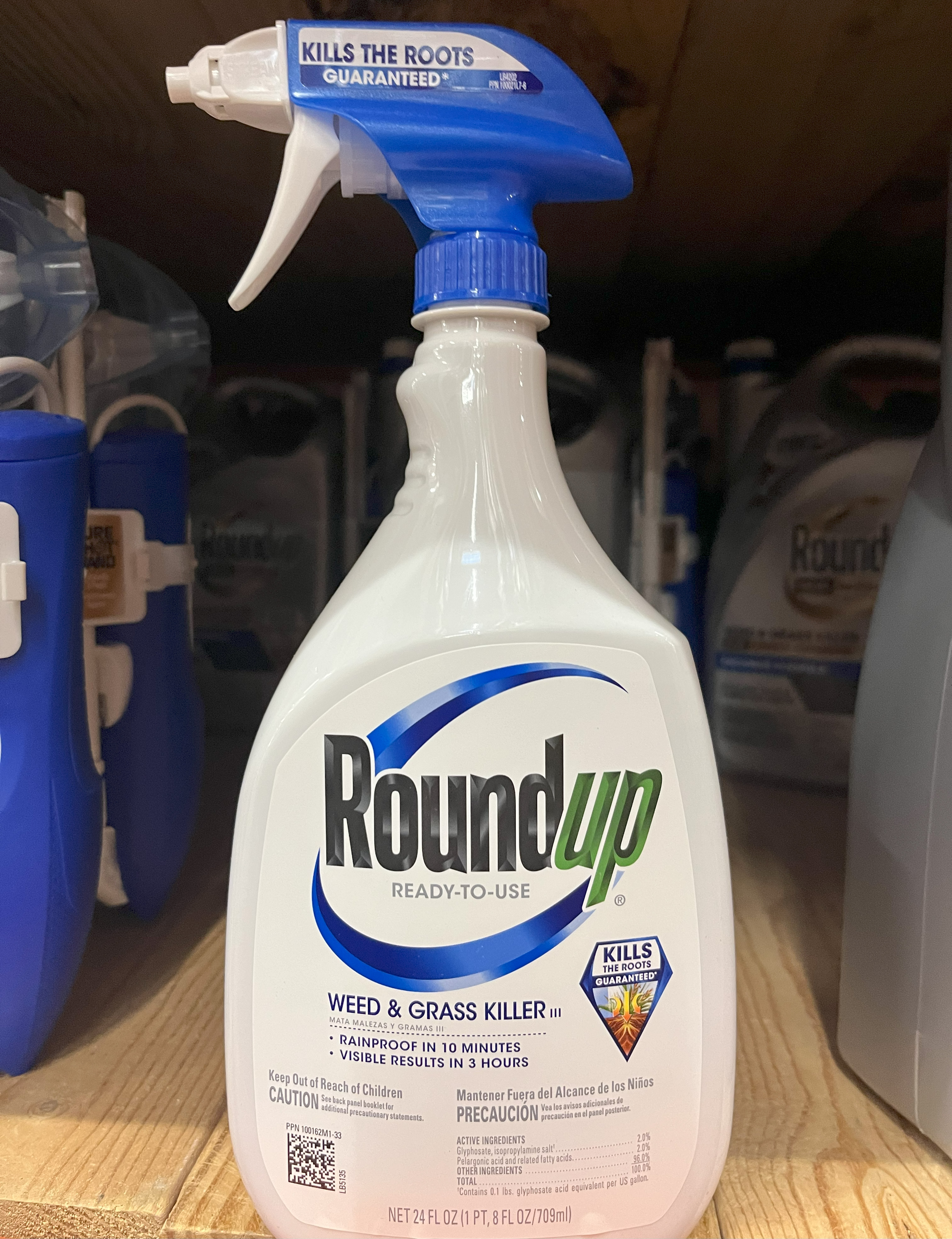 A bottle of Roundup Weed and Grass Killer sitting on a shelf surrounded by other products.
